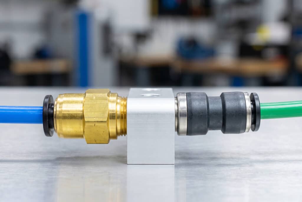 ภาพเปรียบเทียบผลิตภัณฑ์แบบเคียงข้างกัน แสดงข้อต่อแบบกดทองเหลืองพร้อมท่อสีน้ำเงินและข้อต่อแบบคอมโพสิตพร้อมท่อสีเขียว เพื่อเน้นความแตกต่างของวัสดุที่ได้กล่าวถึงในบทความ.